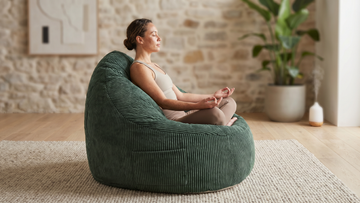 Femme assise en tailleur en position de yoga sur un pouf vert dans un salon bohème naturel