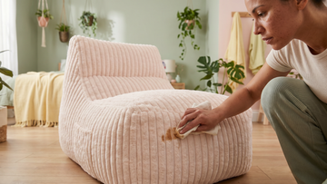 Femme nettoyant son pouf rose pâle en velours tacheté de café  dans un salon bohème moderne