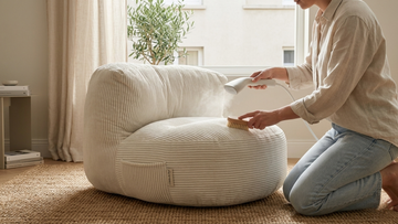Femme qui brosse le tissu de son pouf blanc en velours côtelé petites côtés dans un salon bohème