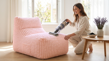 Femme qui nettoie son grand pouf rose pâle avec son aspirateur dans un salon lumineux