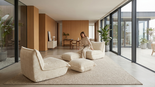 Femme s'apprêtant à s'asseoir sur son pouf en velours côtelé crème avec repose pied dans son grand salon lumineux moderne.